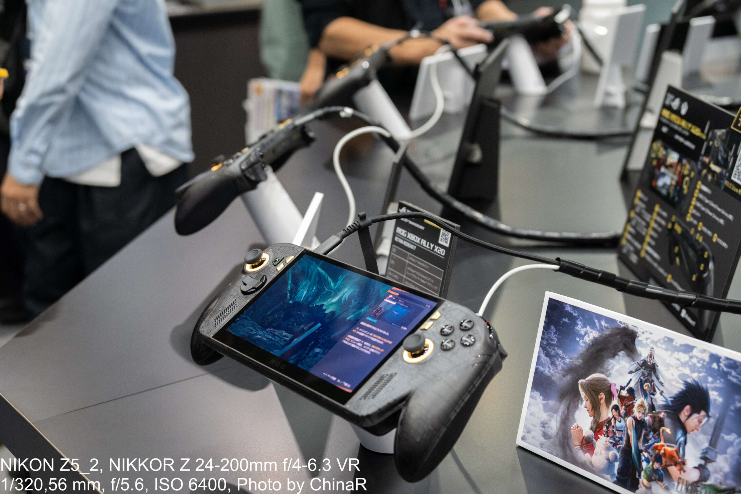 ROG XBOX ALLY X20の実機がスタンドに載った展示。金色リングのスティックと仕様カード、FF7 REBIRTHのアートカード
