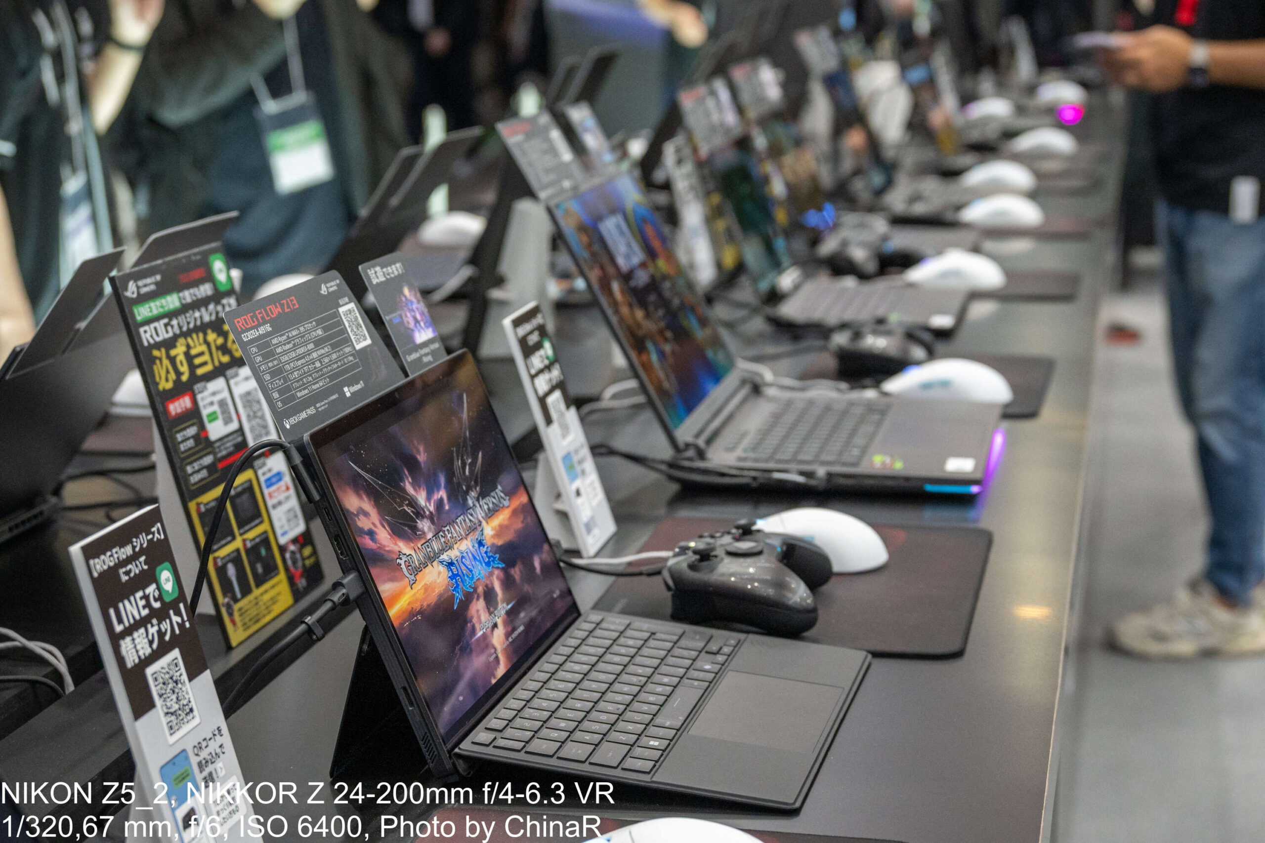 ASUS ROGブースに並ぶ試遊用ノートPCの列。各台にゲームカードとLINE案内、白いROGマウスとXboxコントローラー